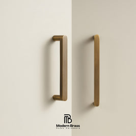 Two brass cabinet handles mounted on a warm off-white wall, with the Modern Brass Home Hardware logo at the bottom.