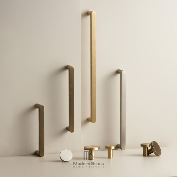 A collection of matte brass and brushed nickel modern cabinet handles in various shapes and sizes, displayed on a clean, light beige wall and surface with the Modern Brass logo at the bottom.