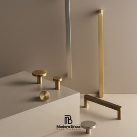 Modern brass cabinet hardware set including round knobs, cylindrical pulls, and bar handles in a brushed gold and satin silver finish, displayed on a minimalist beige platform against a neutral beige background. The Modern Brass logo is visible at the bottom.
