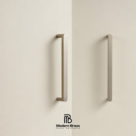 Two matte brass door handles mounted on cream-colored doors, with the Modern Brass logo at the bottom.