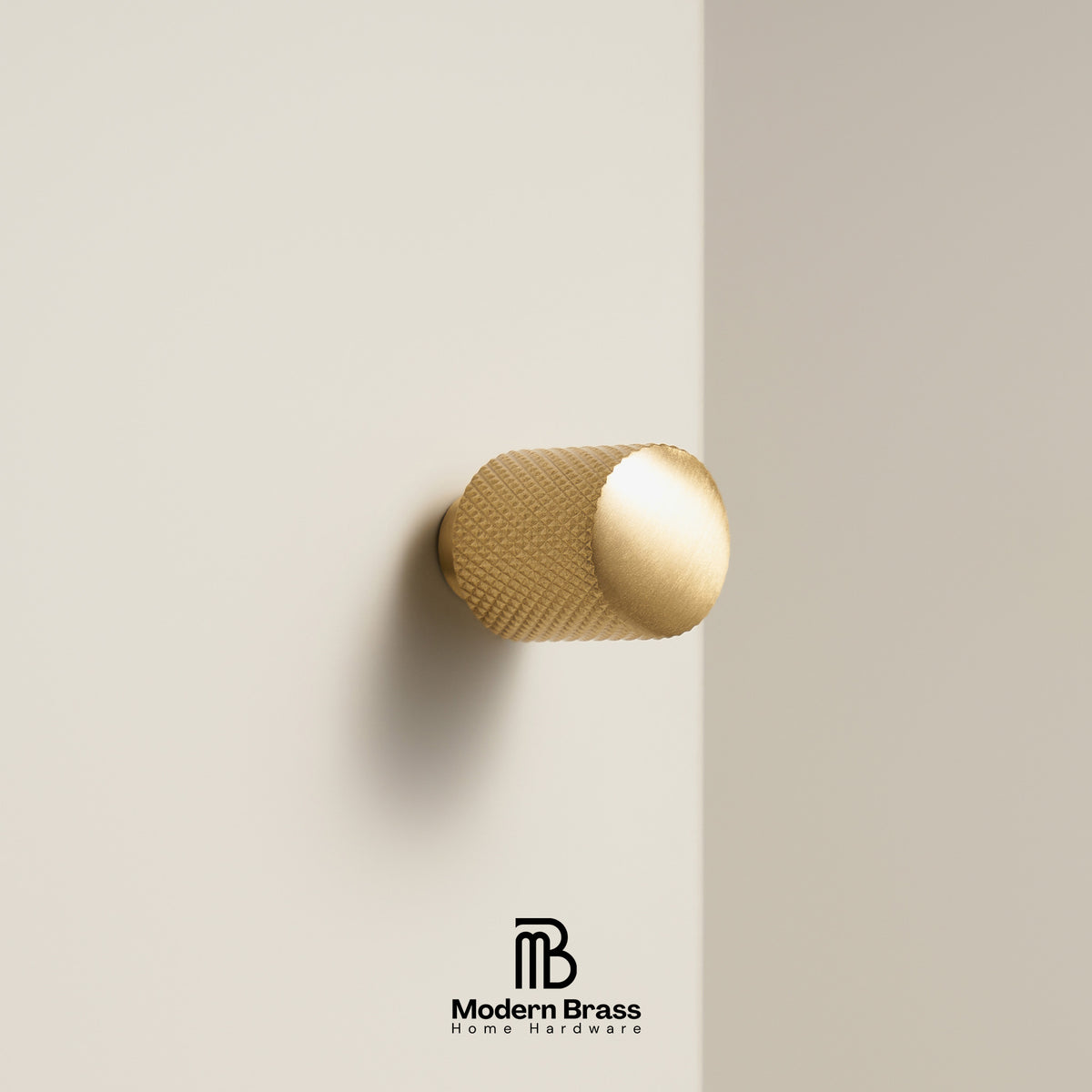 A modern cylindrical brass cabinet knob with a textured knurled surface and a smooth polished end, mounted on a minimalist beige wall. The Modern Brass logo is visible at the bottom.