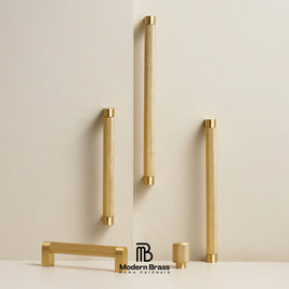 Five brass cabinet handles in various shapes and sizes, displayed on a clean off-white background with a brand logo at the bottom.