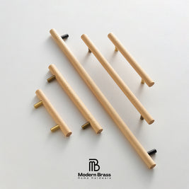 Five modern cylindrical cabinet handles made of light natural wood with brass and black metal end caps, arranged diagonally on a clean white background. The Modern Brass Home Hardware logo is visible at the bottom.
