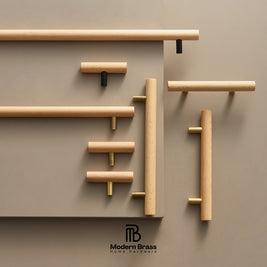 A styled product display of various modern cylindrical wooden cabinet handles in natural oak, mounted on a matching warm taupe wall. The handles feature brass and black hardware accents.